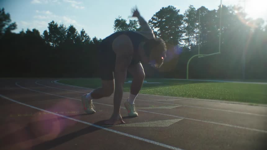 An asian male athlete takes position on a racing track and then begins running