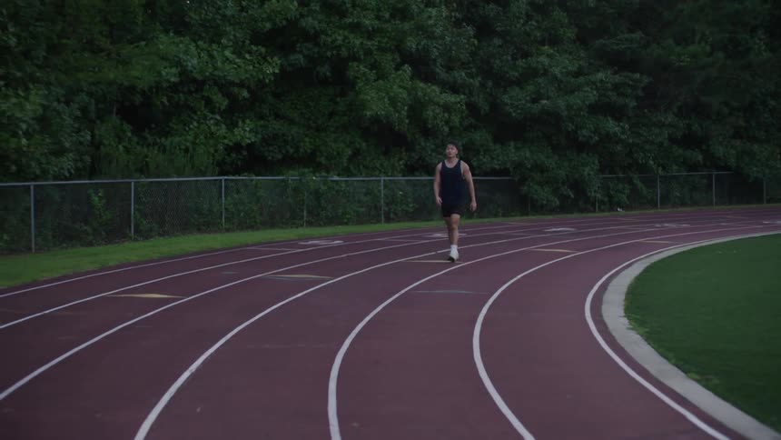 A young man walking on a red colored curved running track