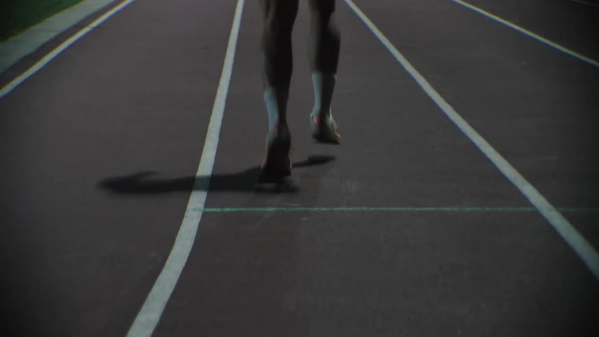 A closeup of a persons lower legs and feet running on a track with marked lanes