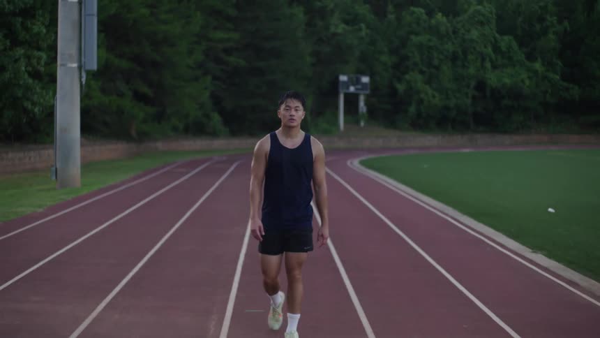 An asian male in athletic attire walks around a racing track in a football stadium