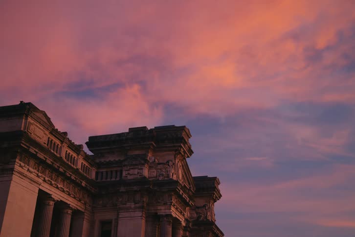 Side of a building with classical architecture against a blue sky with red tones