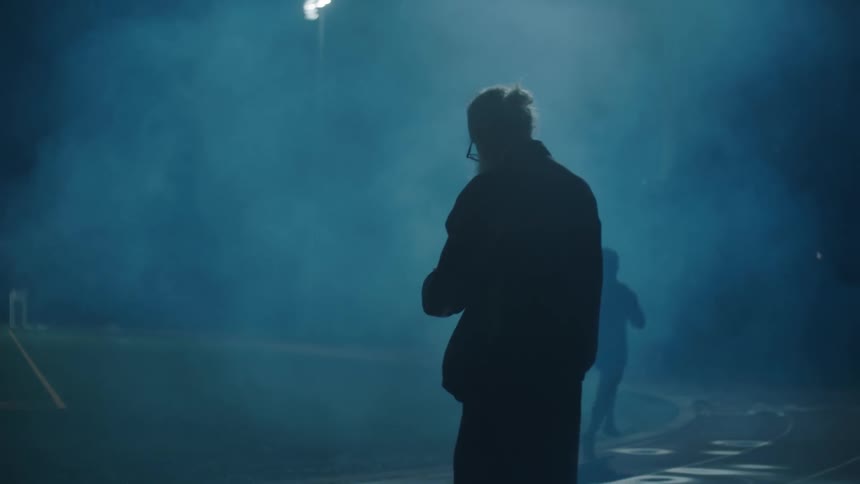 Elderly man timing a young man running on an athletics track at night