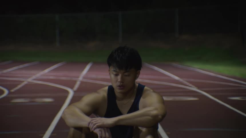 An asian man looks tired as he sits on a track