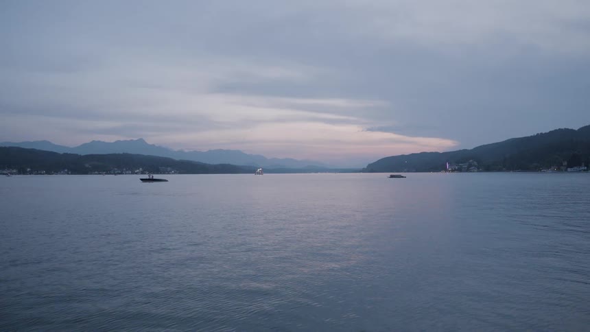 A tranquil body of water with boats and a mountain range under a dusky sky
