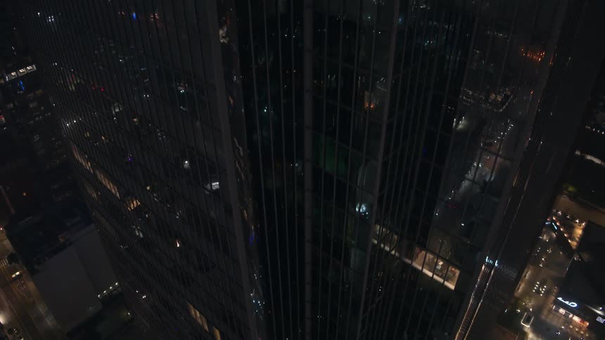 Traveling up a huge building with an exterior full of glass windows in a metropolitan city at night