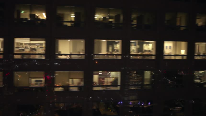 Aerial view of a city at night lit up with some interiors shown through office windows