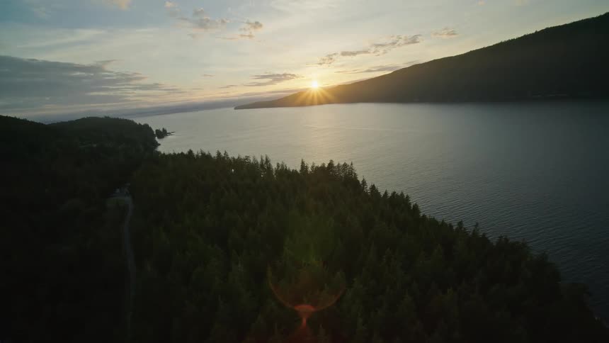 The sun shines over mountains next to a river and a forested rural area