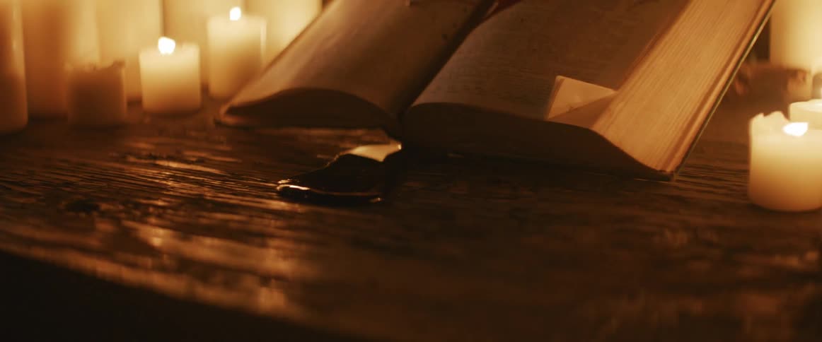 Book on top of a wooden table with blood and candles