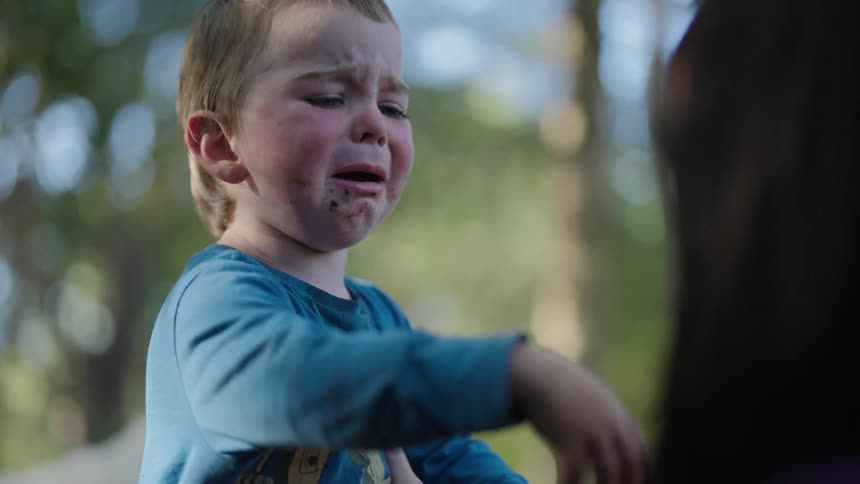 A baby is crying and reaching for his mother