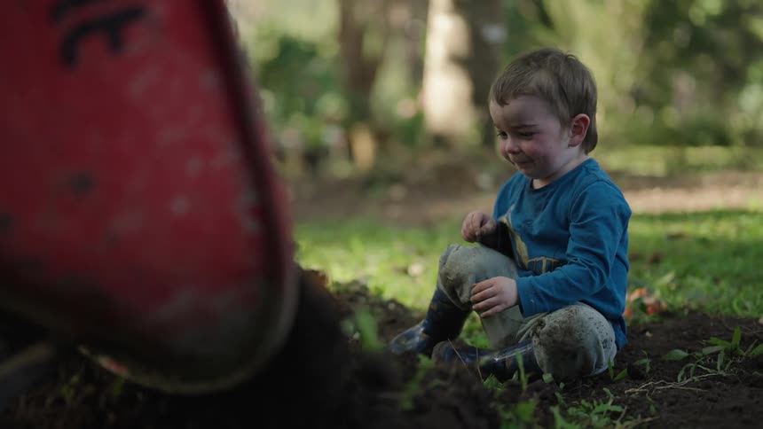 Dog moves forward to stand near a small child watching dirt being emptied from a wheelbarrow