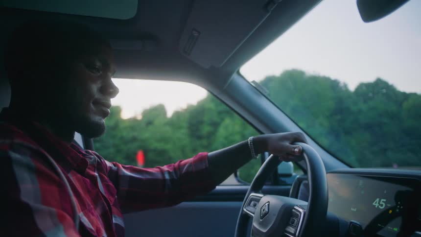The face of a young man who is driving a car holding his hands in front of him looking forward