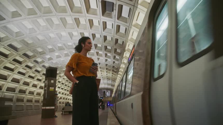 A woman standing next to a subway train that is moving in a terminal