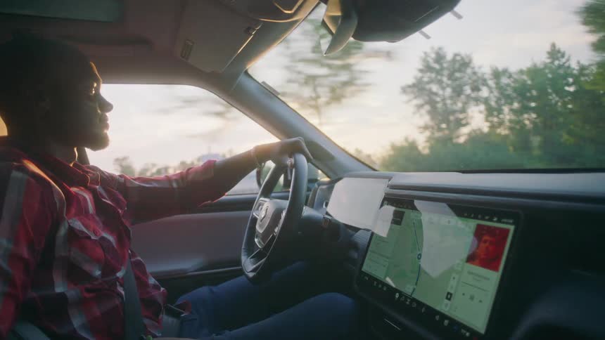 A black man drives his car down a rural road