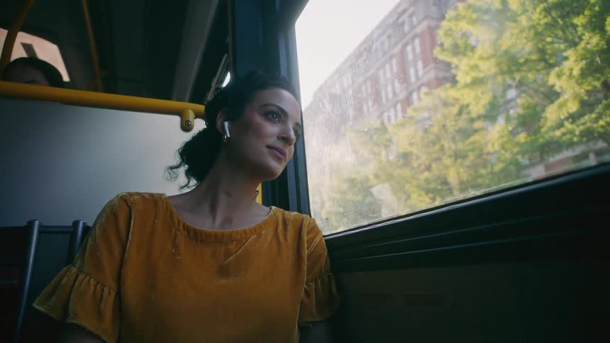 A young woman with ear buds rides through a city on a bus