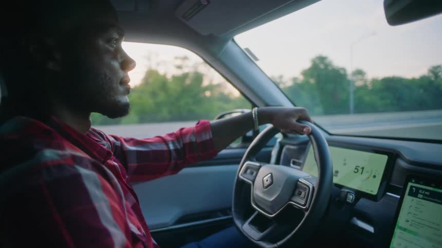 A seated man looking intently ahead as he is driving a car holding his hands on the steering wheel