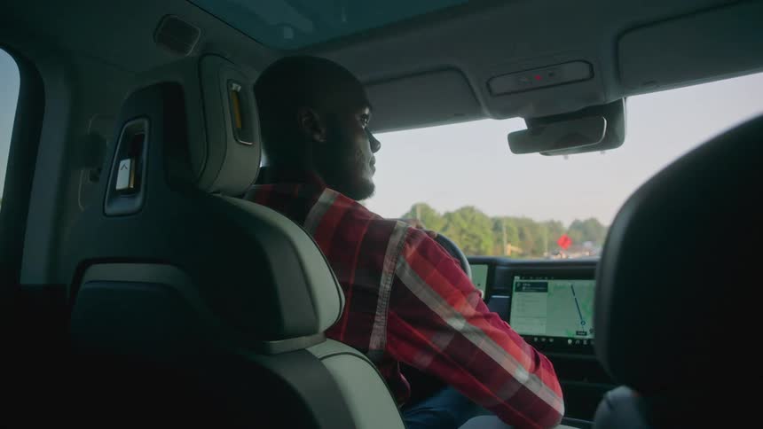 A black man uses a dashboard computer as he drives his car down a road