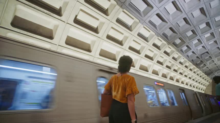 Woman walking inside a station with a train passing by