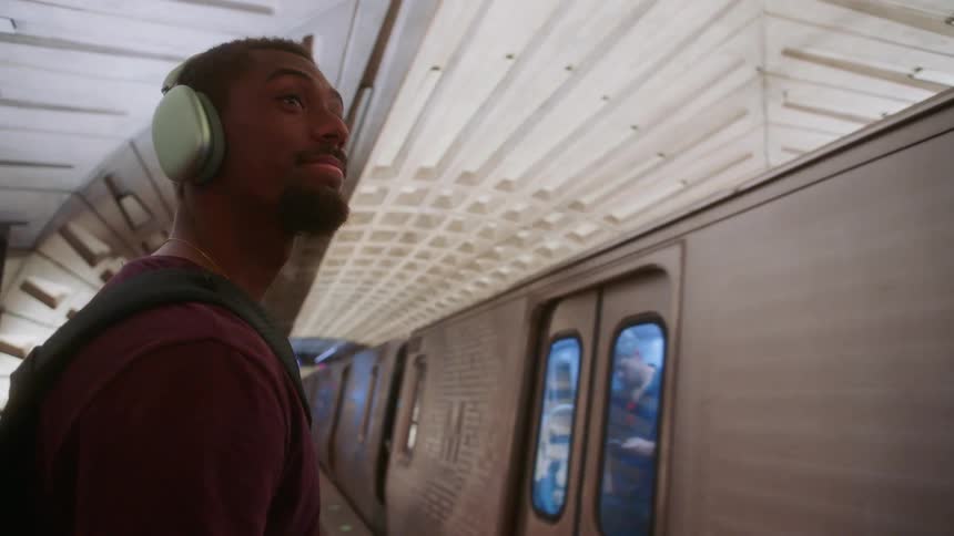 A man wearing headphones is looking at a subway train passing in front of him