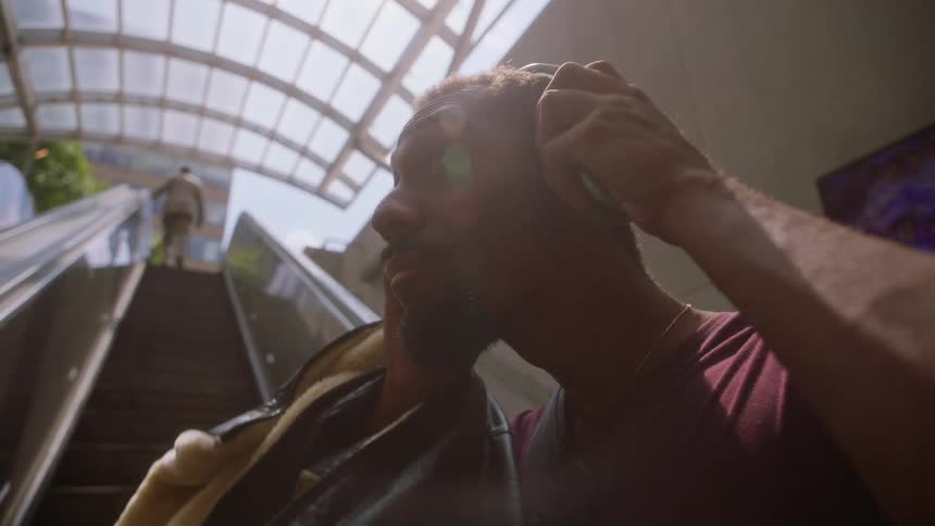 Man going up an escalator and putting on headphones