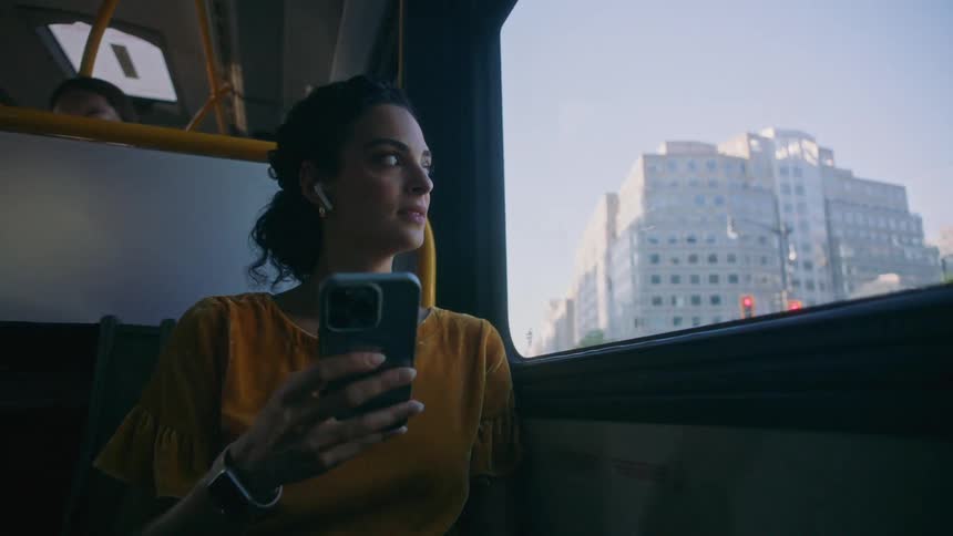 Woman holding an iphone and looking out the window of a moving bus