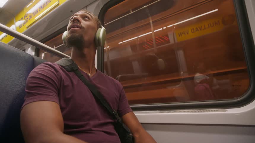 A black man listens to headphones while riding on a subway car