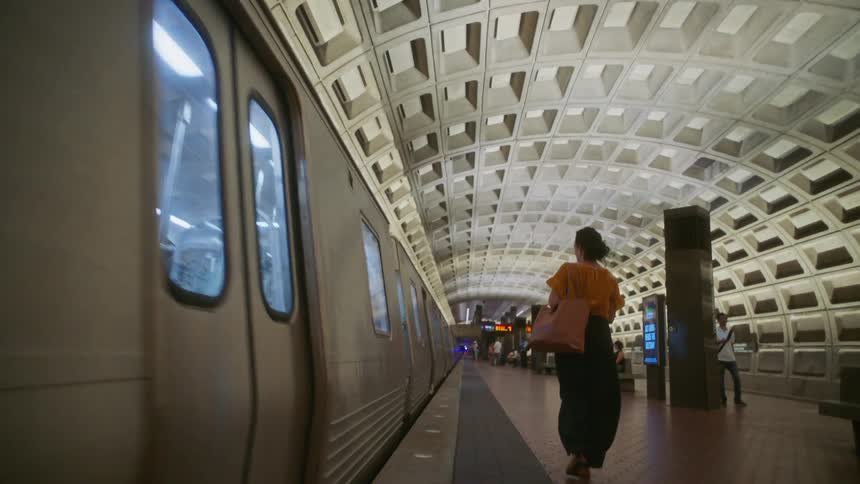 Back view of a woman walking next to a train in a subway