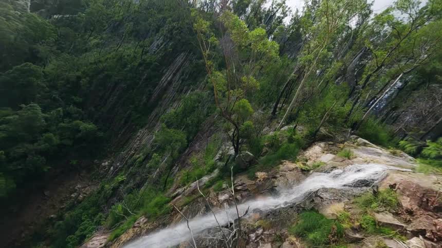 An aerial view of flying down a woodland waterfall