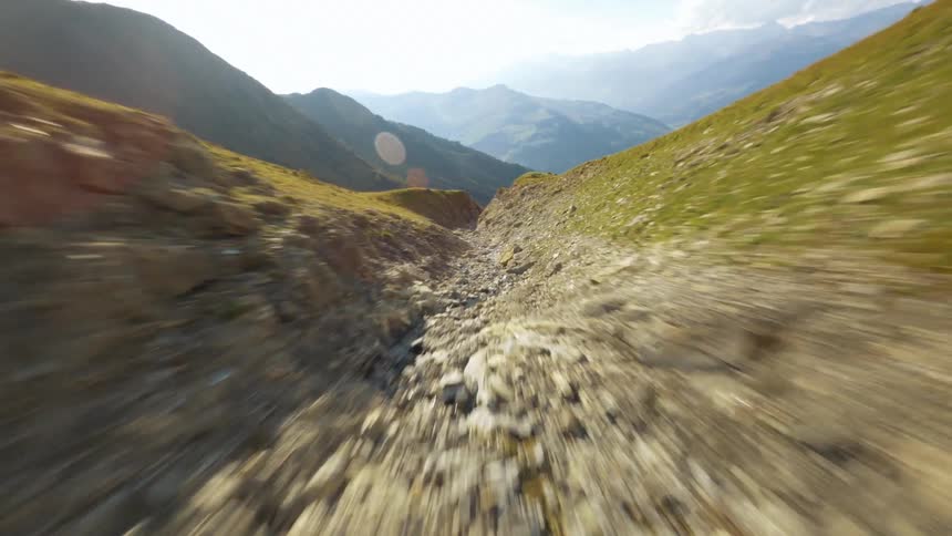 Flying down a dry river bed going down the grassy mountain