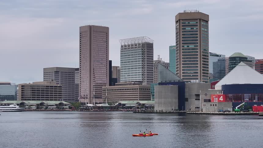 A city skyline with highrise buildings and a river in the foreground where two people are kayaking