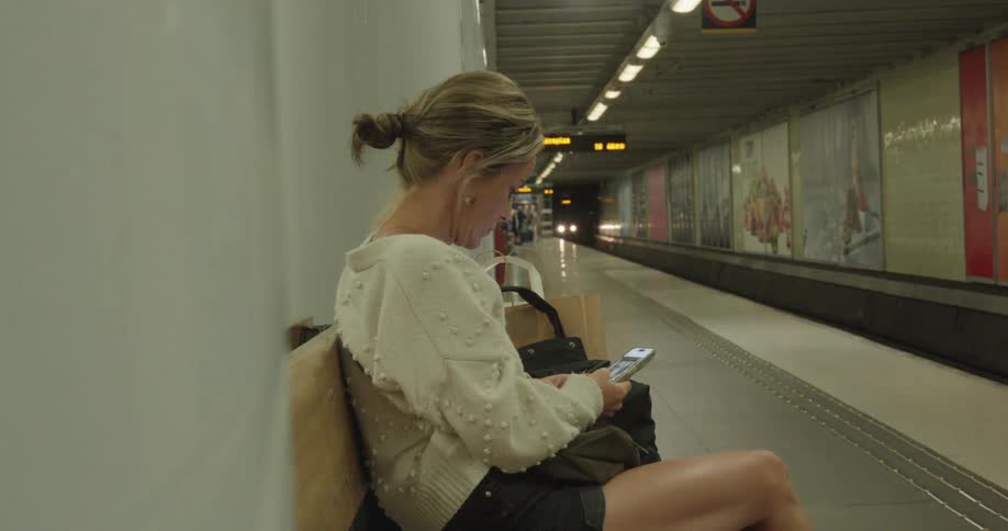A young woman sitting in a subway station using her smart phone while the train arrives
