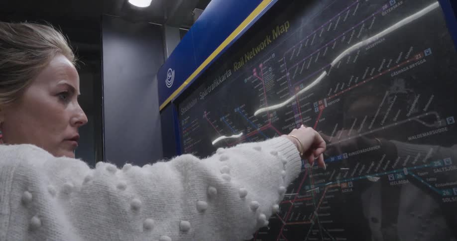 A woman traces her finger over a map in a train terminal