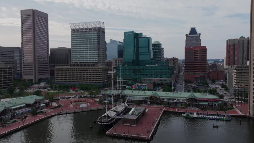 Large sailing ship sits docked at waterfront located near downtown on a cloudy day