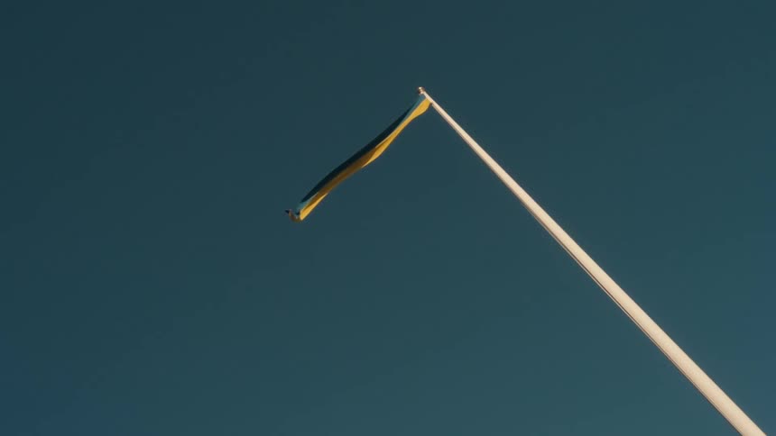 A blue and yellow banner blows in the wind atop a long metal pole