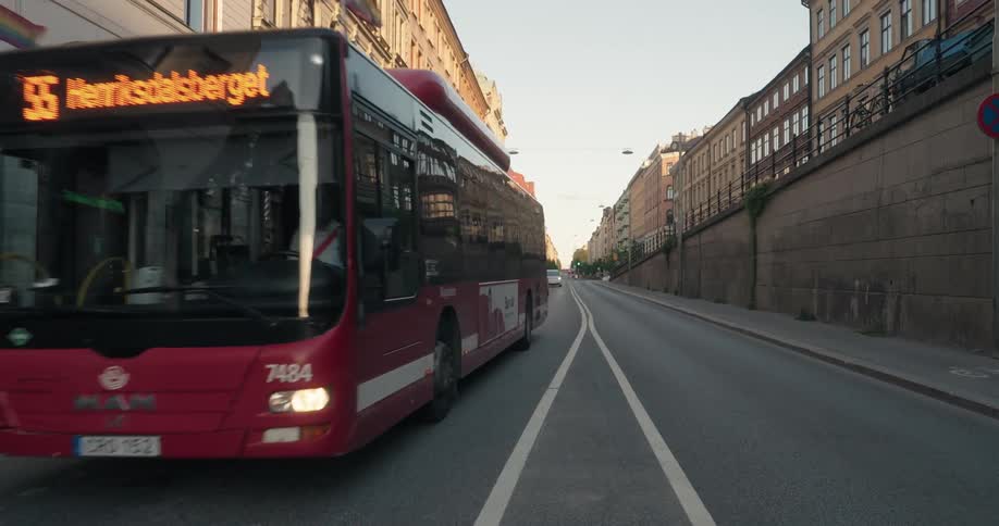 A red city bus drives down an empty urban street with tall buildings on either side