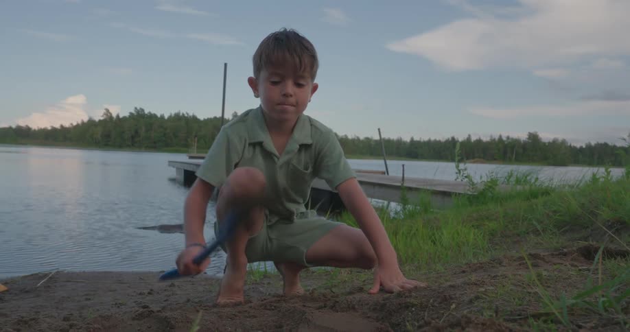 Little child playing in the dirt by the lake