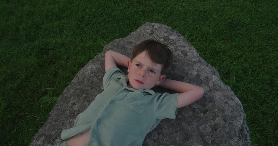 Boy lies on a boulder looking upward on a summer day