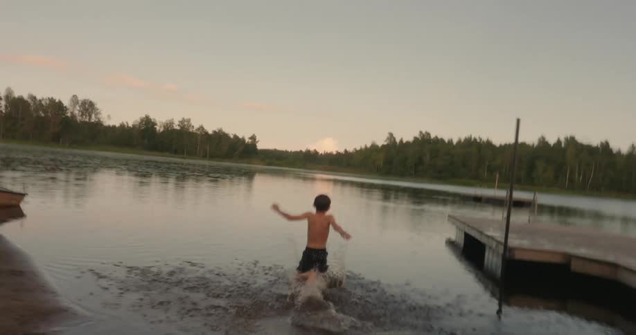 Boy running and jumping into a lake in the late afternoon