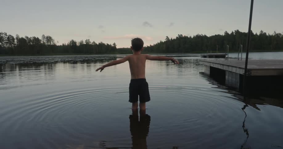 View of a boy from behind playing in a lake in the late afternoon
