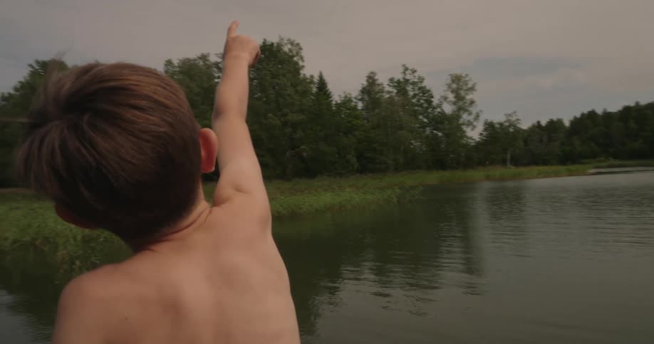 Boy on the shore of a lake pointing up