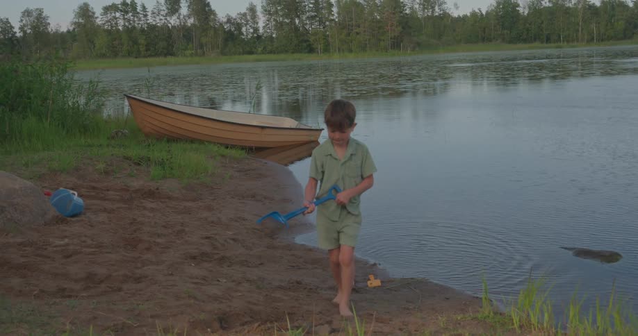 Boy scoops up mud from the bottom of the pond and deposits it on shore