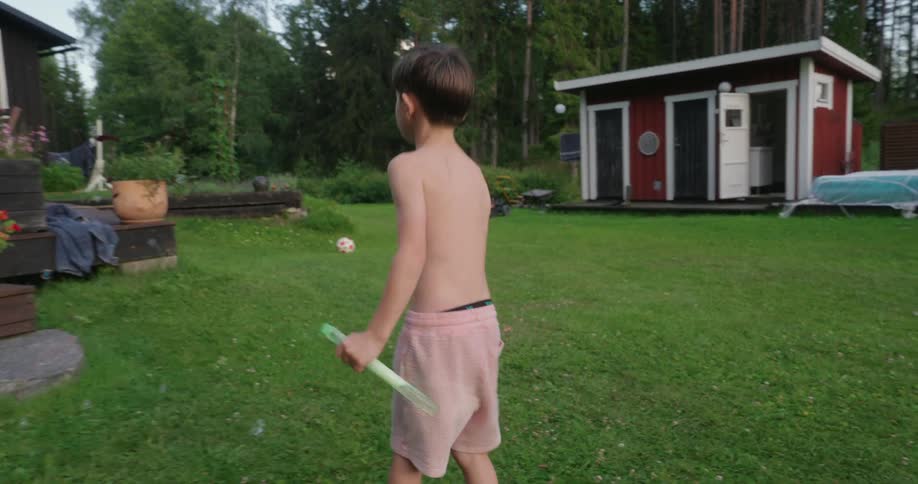 Boy uses a wand in soapy water to create bubbles in the yard