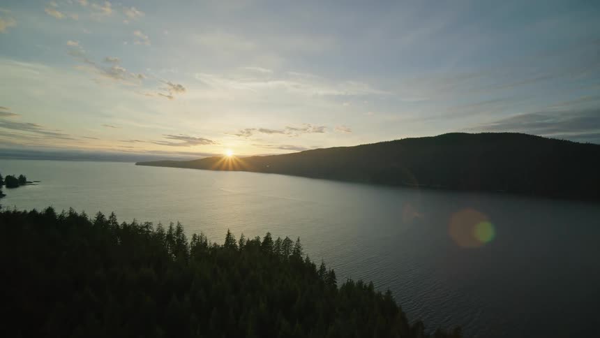 Rising sun shines across forested mountain under a slightly cloudy sky