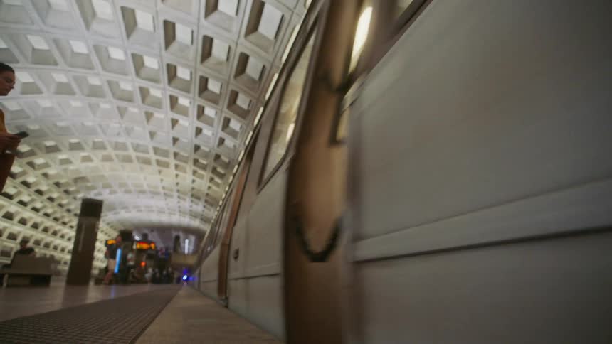 An interior view of a metro station with a curved coffered ceiling tiled walls and a train leaving the station