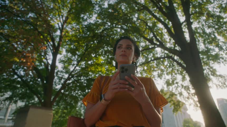 Woman interacting with a smartphone and walking through the streets of a metropolis with trees in the background
