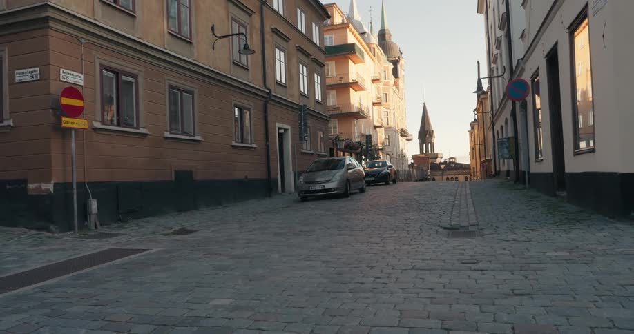 Two cars are parked in front of tall city buildings on a cobblestone road