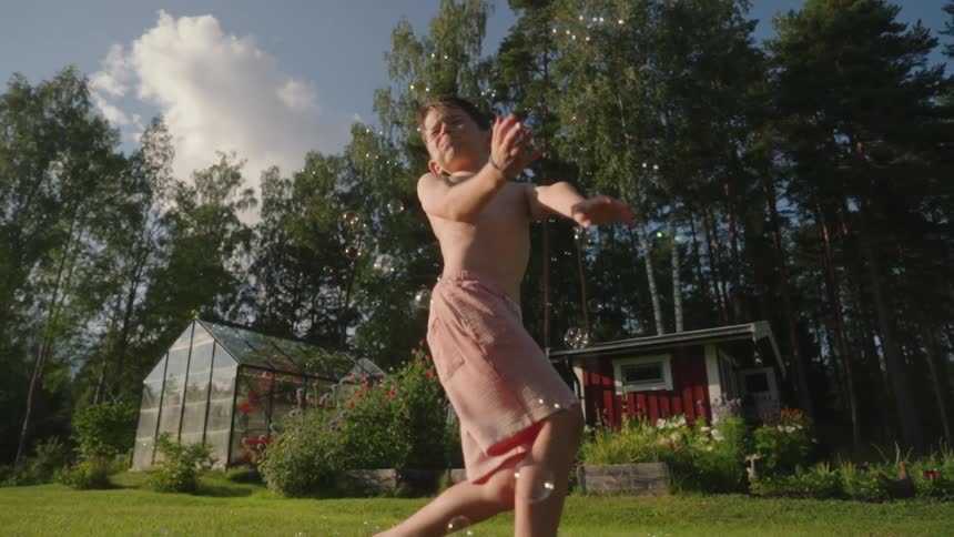 A young boy chases water bubbles in his backyard on a summer day