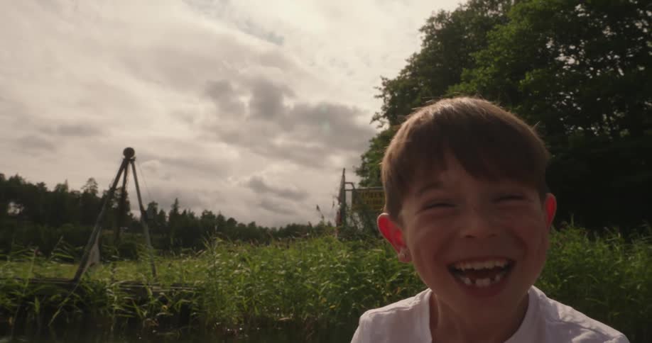 Boy sitting near the water laughs and gestures while talking on an overcast day