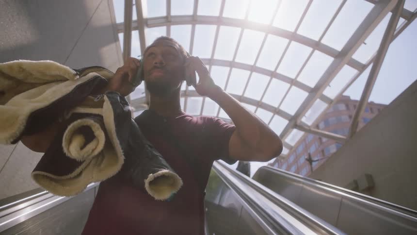 Man riding on an escalator puts on over ear headphones on a sunny day