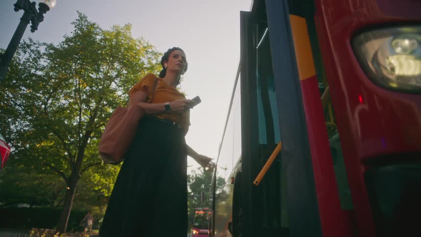 A woman with a smartphone and bag follows another person into a bus