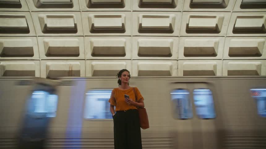 Woman inside a terminal typing on her smartphone and a train passing by in the background